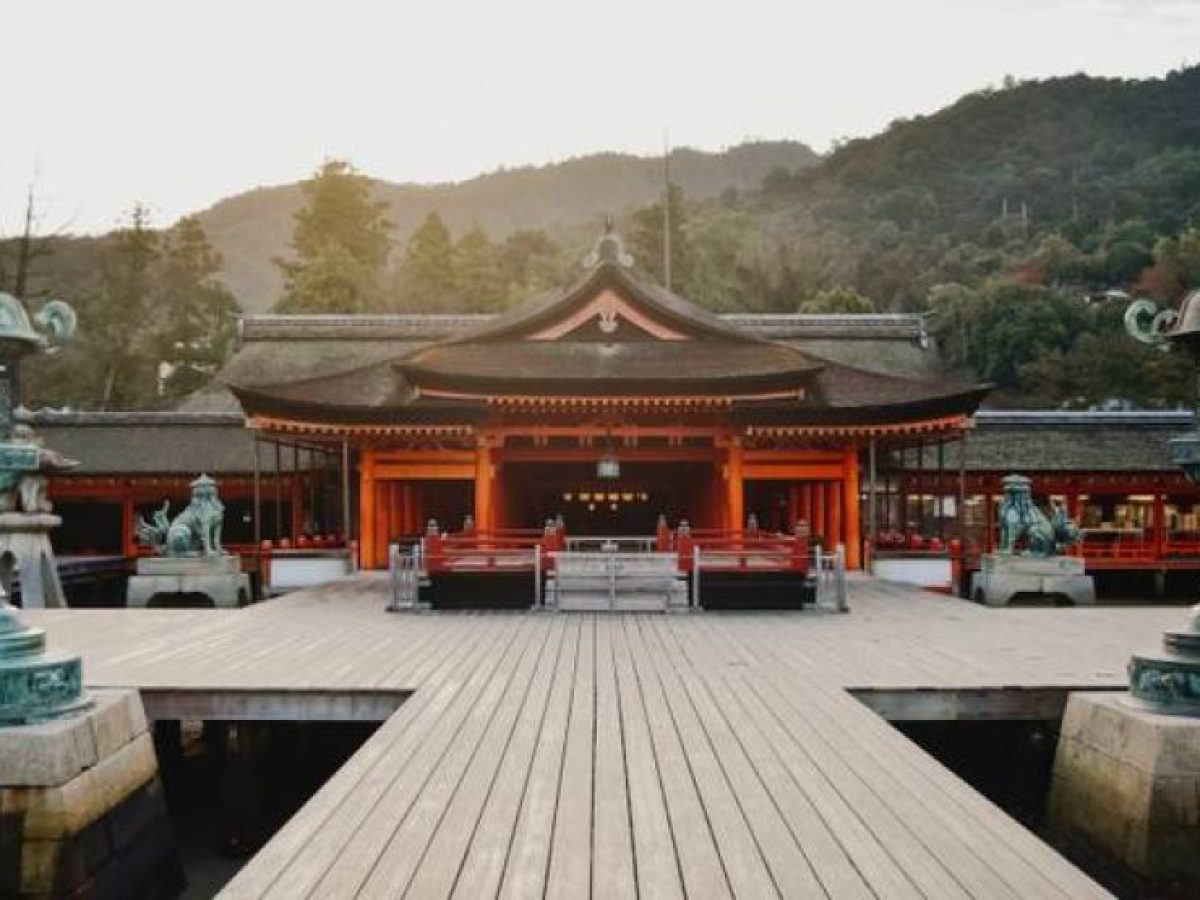 Epic Japan tour view of a traditional Japanese shrine with red wooden architecture, lanterns, and mountain backdrop.